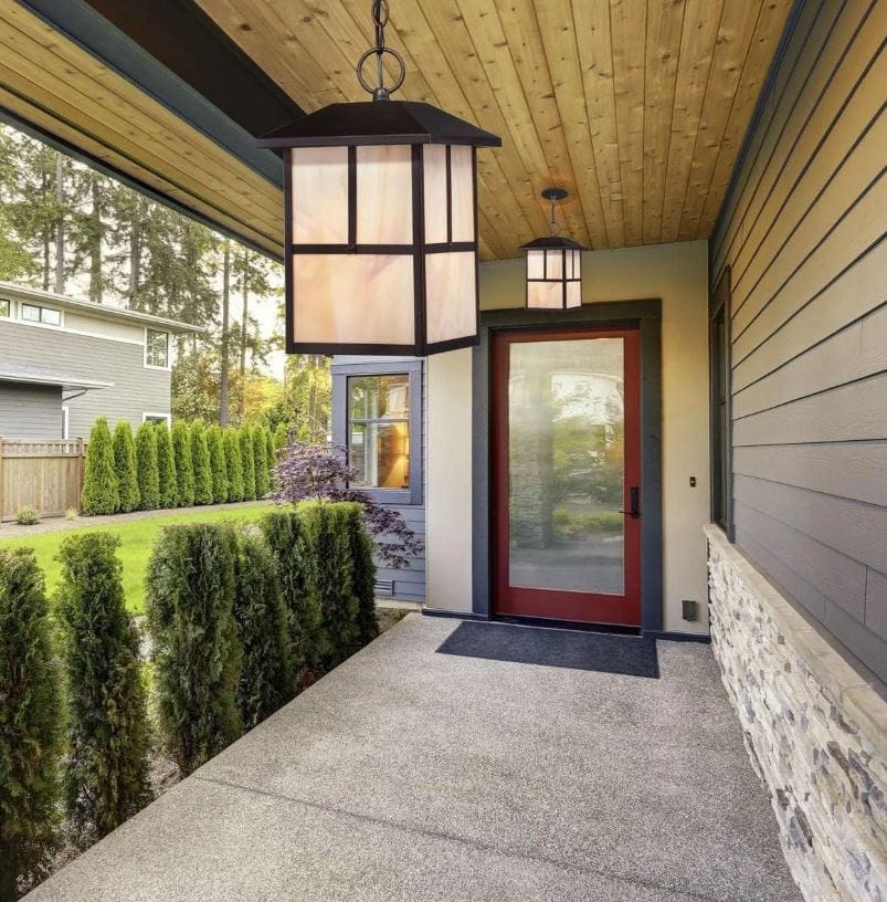 Amazon outdoor lighting deals; Traditional hanging lanterns on a front porch hanging over the entryway to the front door with shrubs on one side and gray siding on the other; elegant outdoor lights