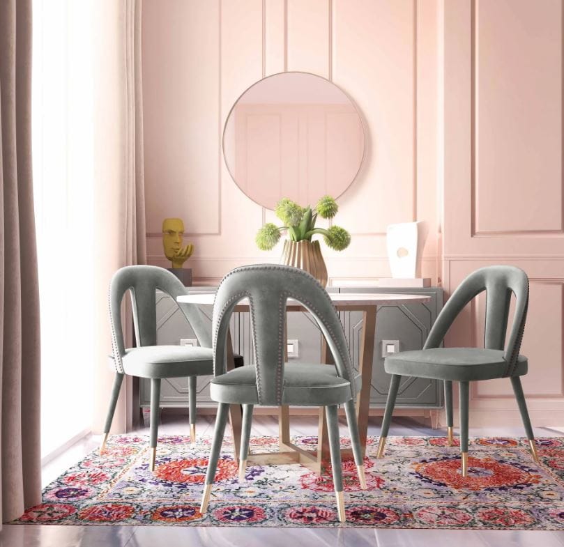 Light grey velvet side chairs with gold tipped legs around a circle dining table on a red and purple rug in a room with pinks walls and a grey sideboard; contemporary accent chairs for dining room; English Elm accent chairs