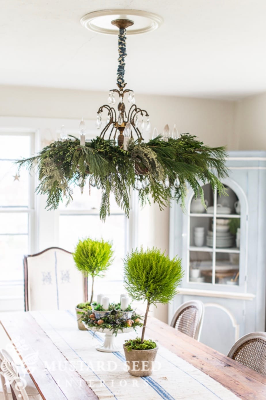 Simple chandelier with greenery placed throughout in a farmhouse style dining room