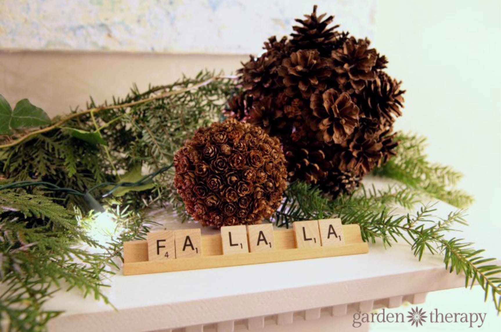 Scrabble tiles spelling Fa La La on a letter holder next to Christmas greenery and pinecones