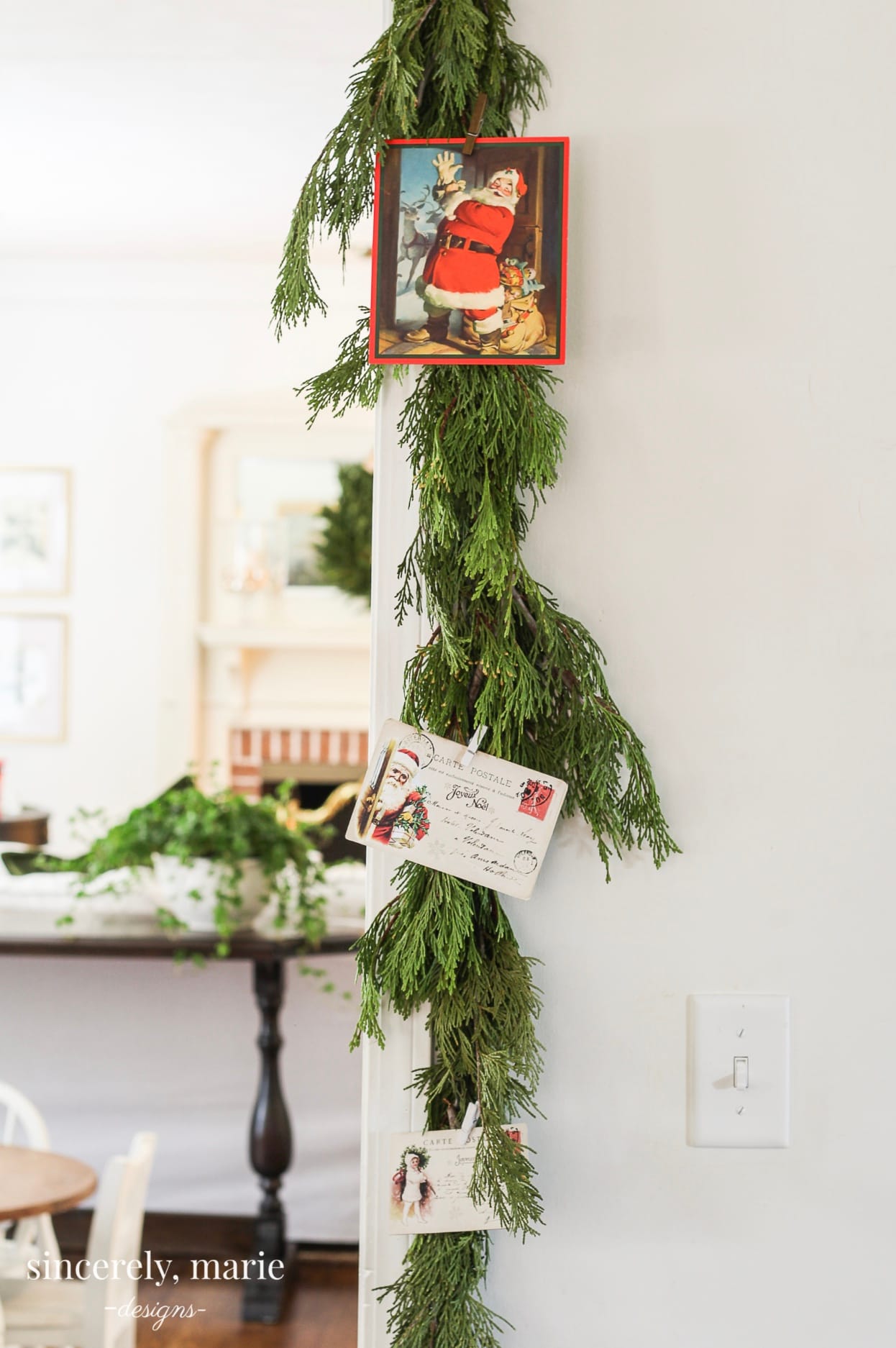 Fresh natural greenery hangs beside a doorway with postcards and a photo of Santa Claus clipped to it