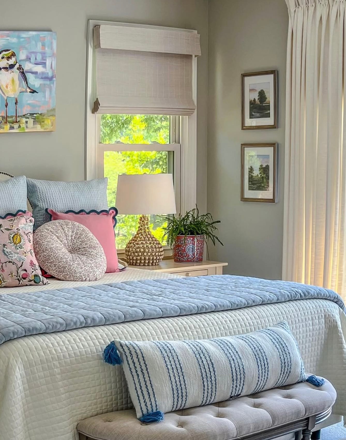 Bed with pastel blue and pink quilt, thrwo pillows, and a coastal design scheme