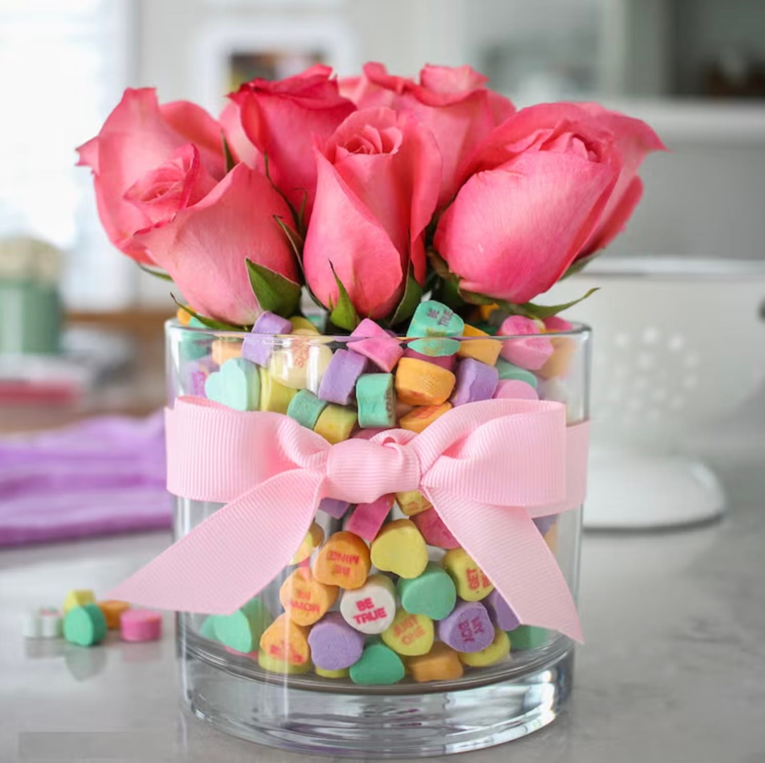 candy conversation hearts in a glass with a bouquet of pink roses