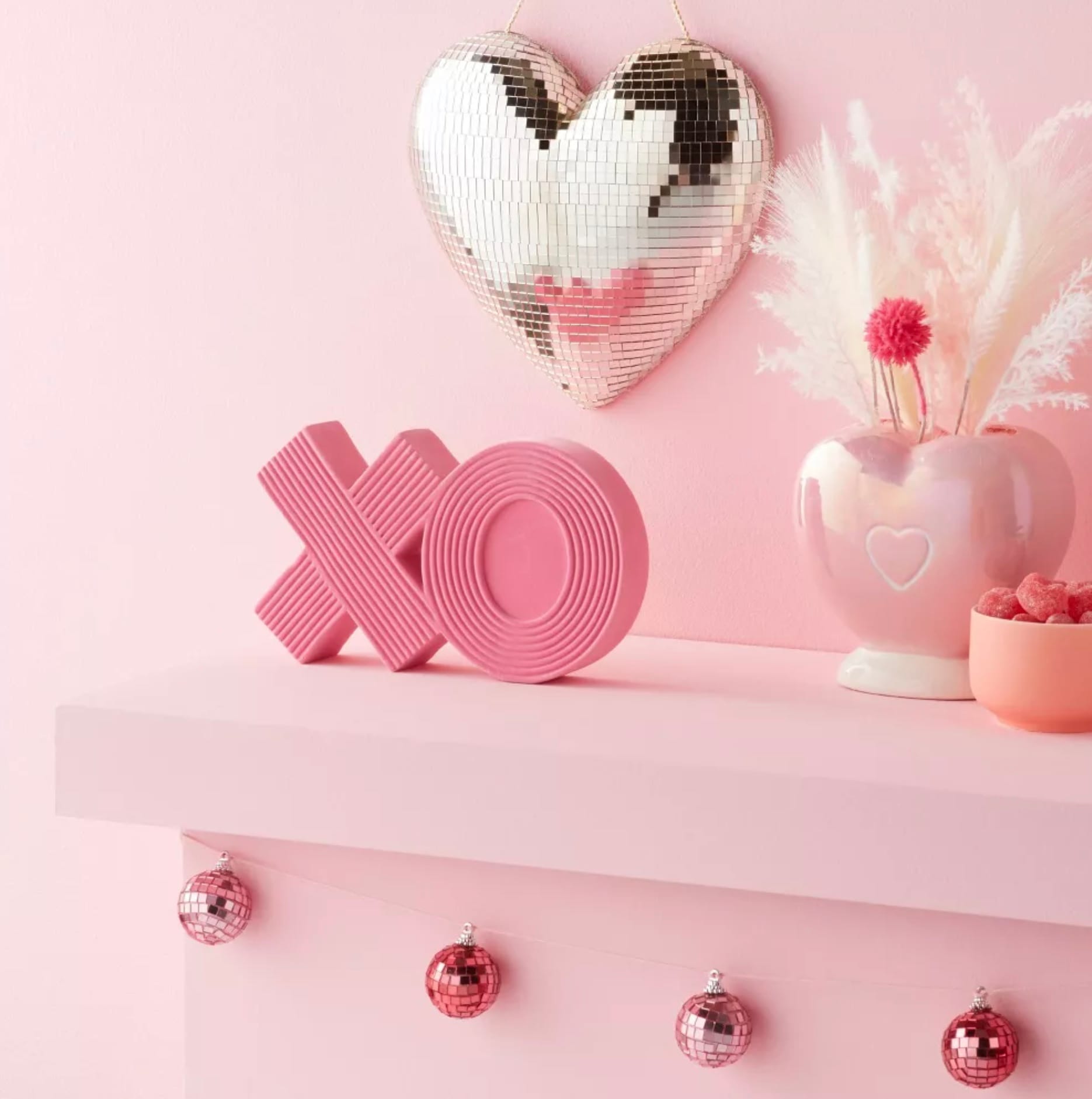 Valentine's Day Heart-shaped disco ball and XO decoration on a mantel lined with pink ornaments