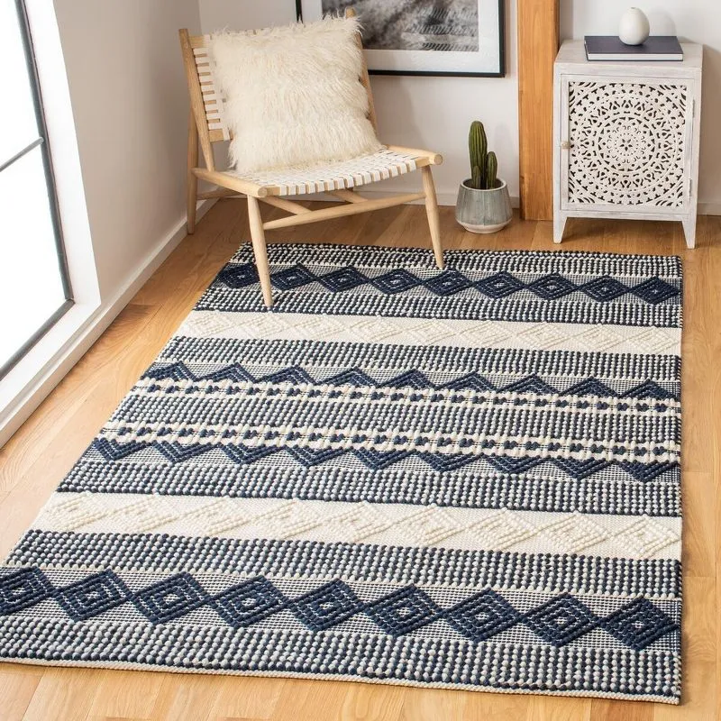A blue and white handwoven Southwestern rug on the floor beside a woven chair and boho nightstand