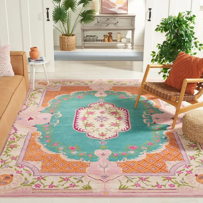 A blue, pink, and orange area rug on the floor beneath a camel colored sofa and woven accent chair