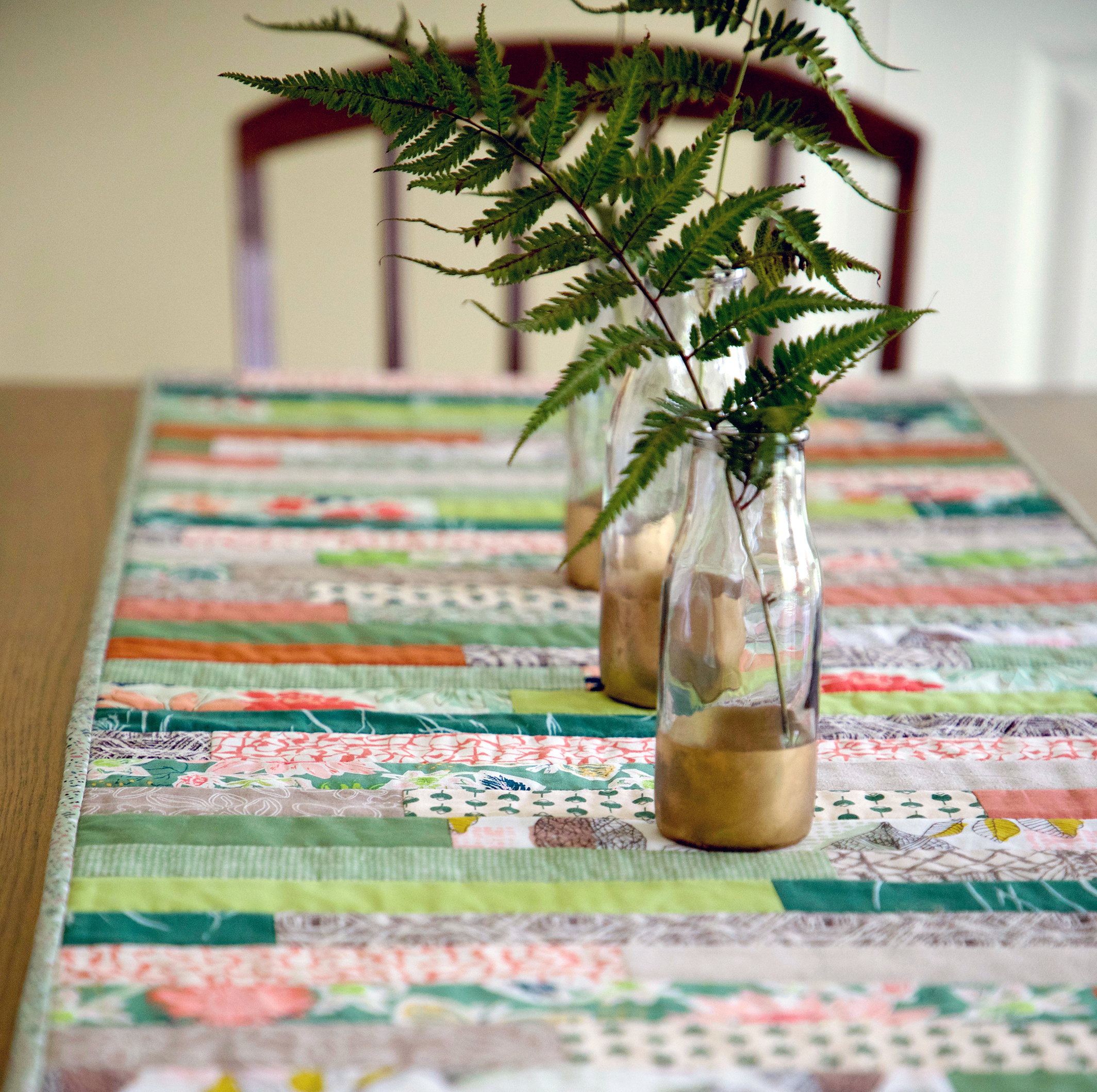 A green, white, and orange table runner on a wooden table with glass jar centerpieces