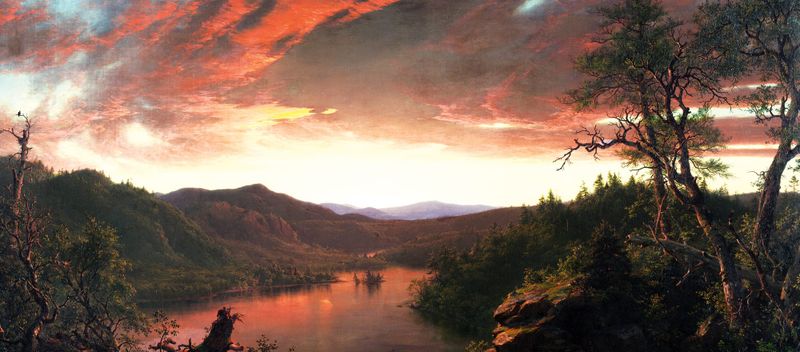 Sunset illuminates a lake and forested mountains beneath a glowing red and gold sky.