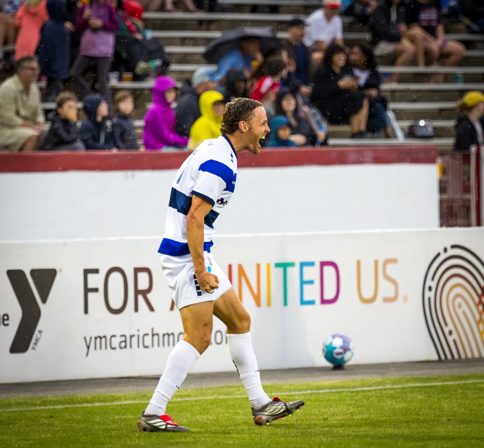 Charlotte Independence player Clay Dimick celebrates after assisting on a goal. The setting is a soccer stadium in Richmond, with the away crowd in the background, in the rain.