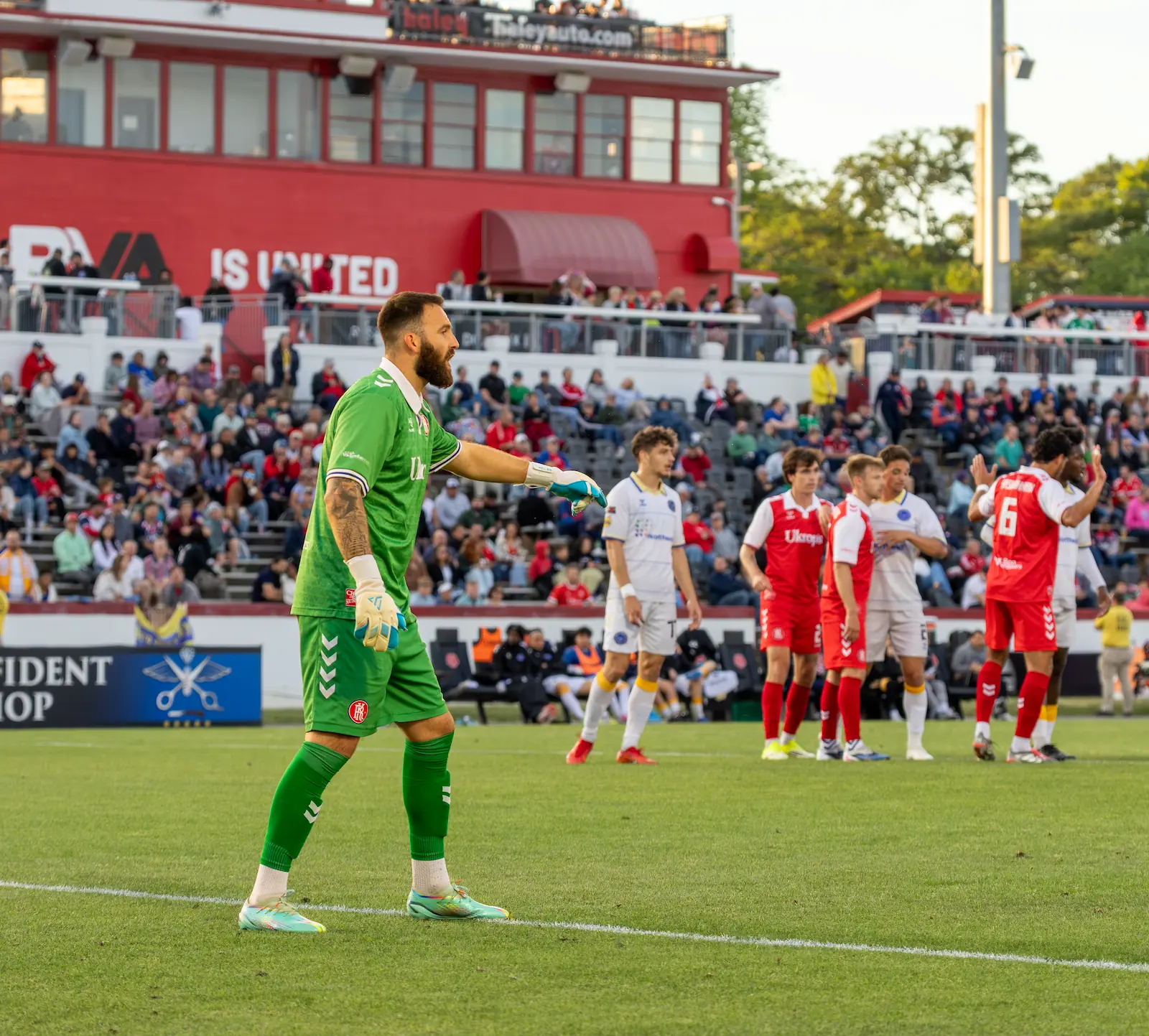 Richmond goalkeeper Yann Fillion directs his teammates during a match against Westchester. The background is a full stadium and players from both teams.