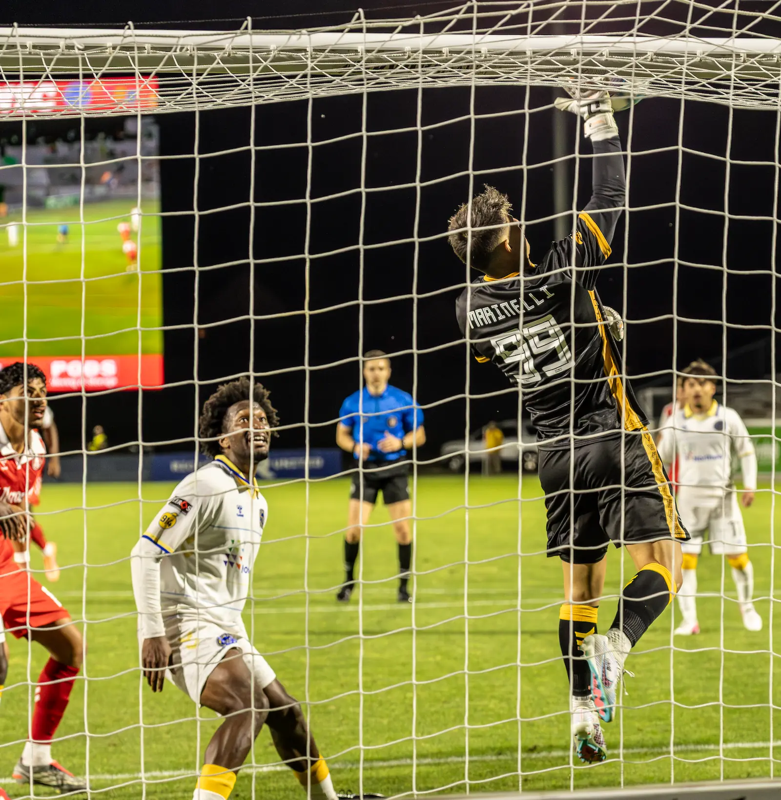 A photo taken from behind the goal shows Westchester SC goalkeeper Luca Marinelli jumping to save a shot while defender Bobby Pierre looks on