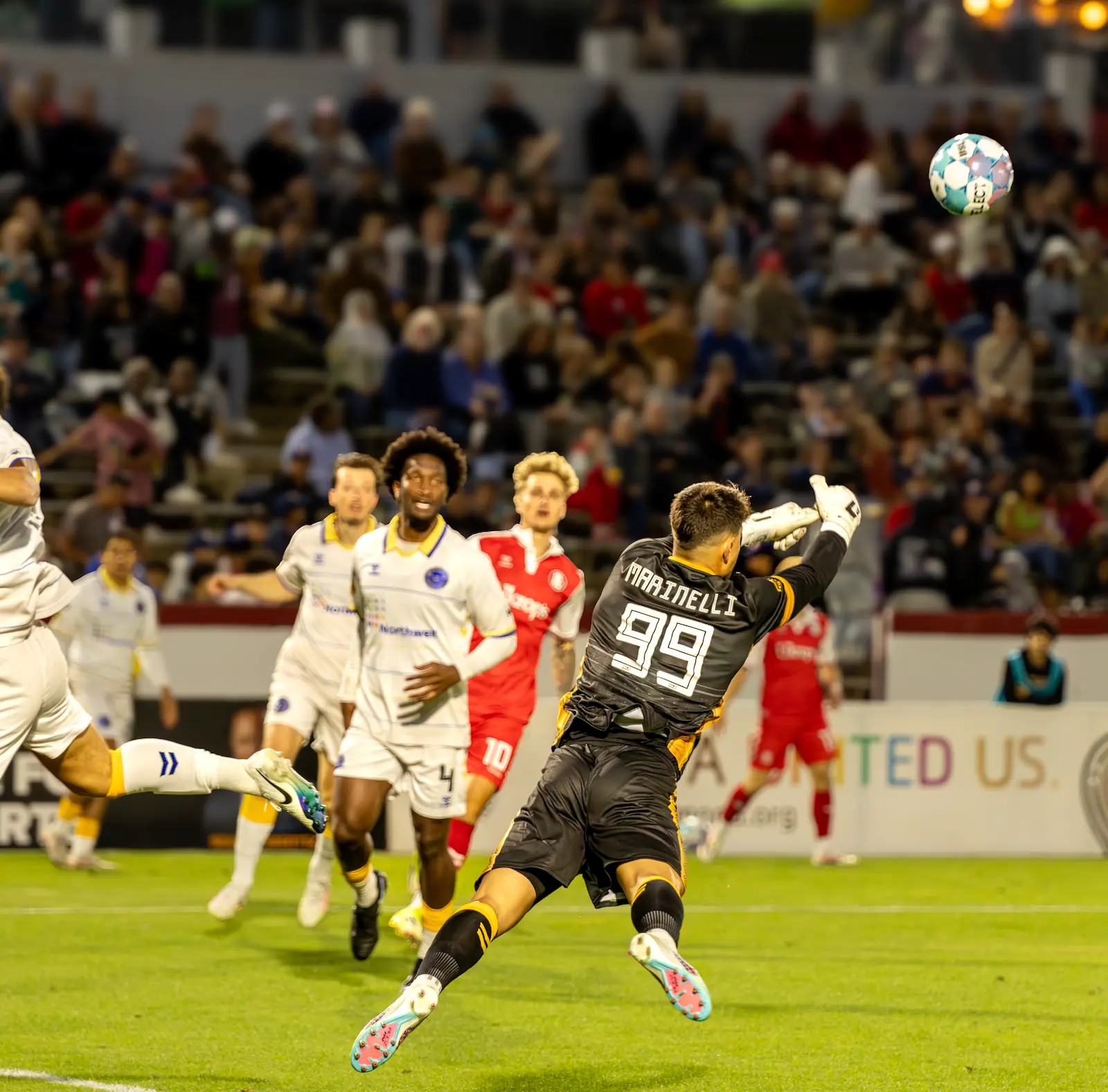 Westchester SC goalkeeper Luca Marinelli dives for a save during a soccer match while teammates and opponents look on
