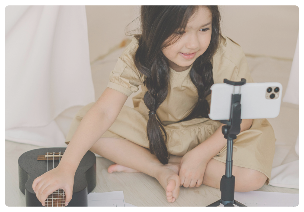 A young girl learning to play an instrument with the help of a smartphone video, showing how active screen time can support music practice and skill-building.
