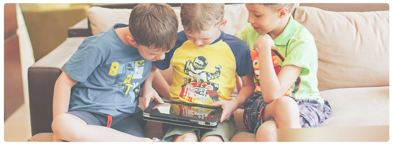 Three young kids sitting on a couch looking at a tablet together, modeling shared screen time and the difference between passive and interactive digital experiences.