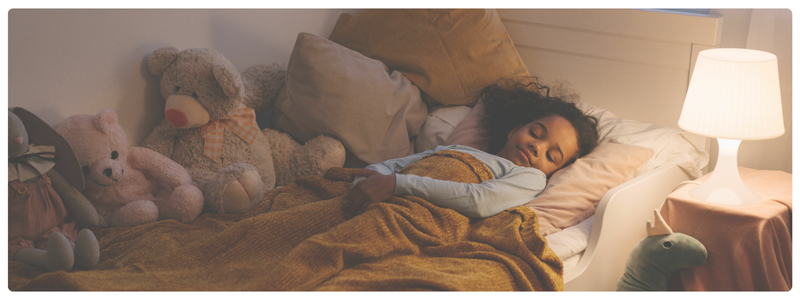 A young child sleeping peacefully in bed surrounded by stuffed animals and soft lighting, illustrating healthy bedtime routines and restful sleep for kids.