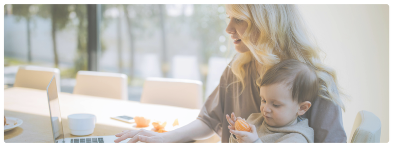 A parent working on a laptop while a young child beside them peels an orange and watches a tablet, illustrating everyday screen time moments and digital parenting balance.