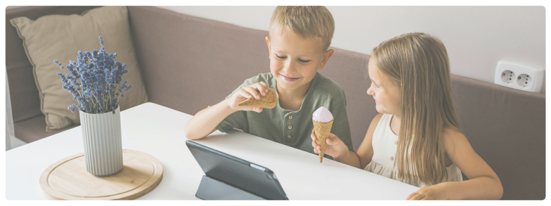 Two children eating ice cream and watching a tablet together, sharing a moment of connection.