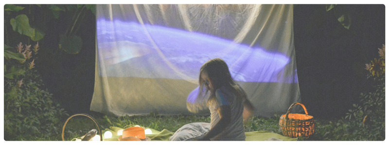 Child sitting outdoors in front of a glowing projector screen on a summer evening, symbolizing balanced screen time during unstructured play.