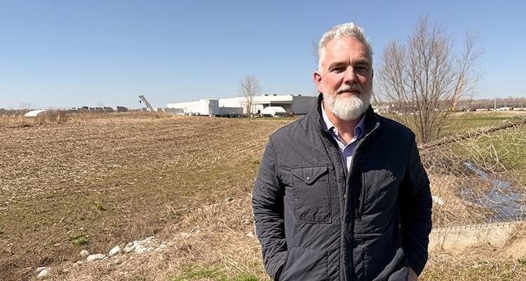 Jeff Brown stands in a field near a building