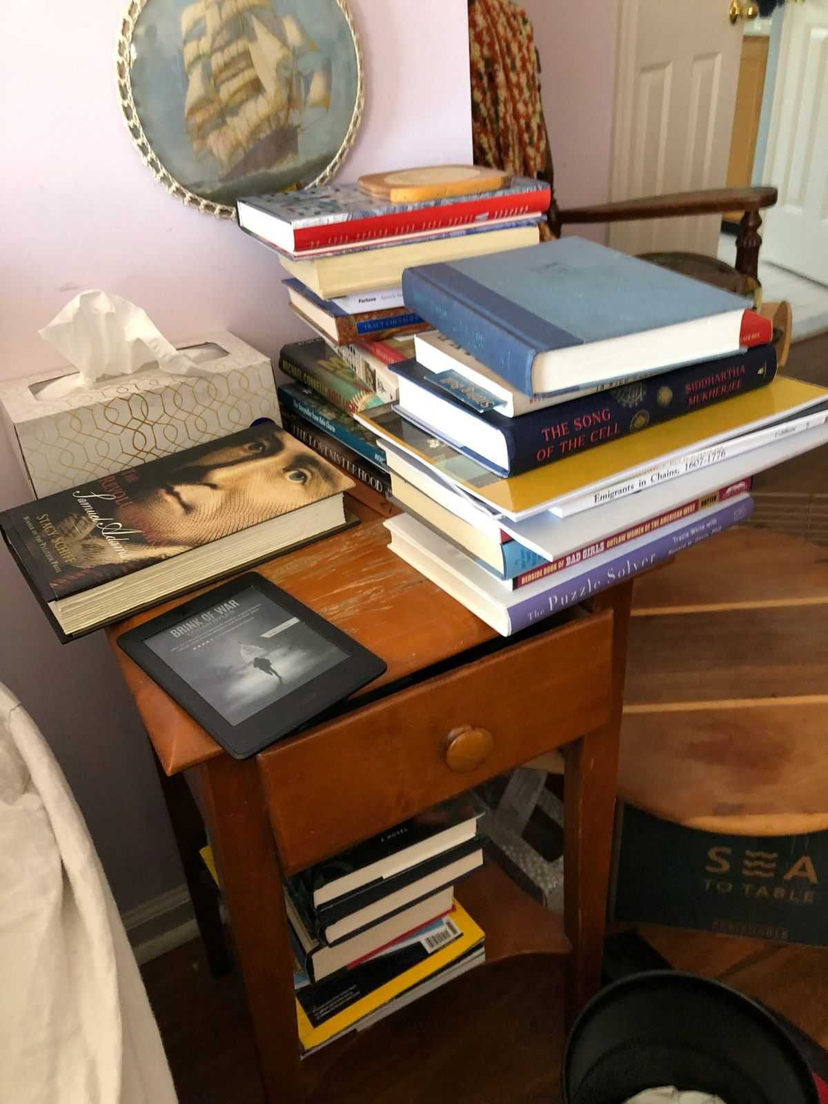Books, an e-reader, and a box of Kleenex are piled on a nightstand.