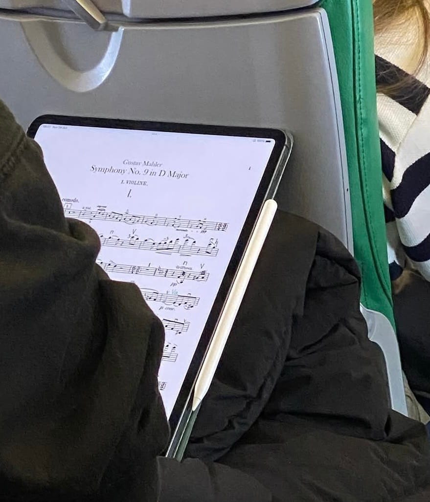 Image of a tablet propped up in front of a passenger on a plane. The screen shows sheet music for a classical music composition. At the top of the screen are the words 'Gustav Mahler' then 'Symphony No. 9 in D Major'