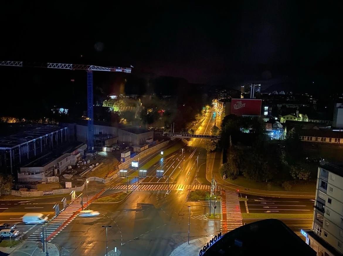 View of a junction at night from above. There is a crane on the left hand side. The roads below are empty, except for four vehicles in traffic in the bottom left corner.