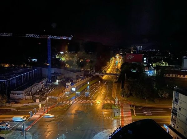 View of a junction at night from above. There is a crane on the left hand side. The roads below are empty, except for four vehicles in traffic in the bottom left corner.
