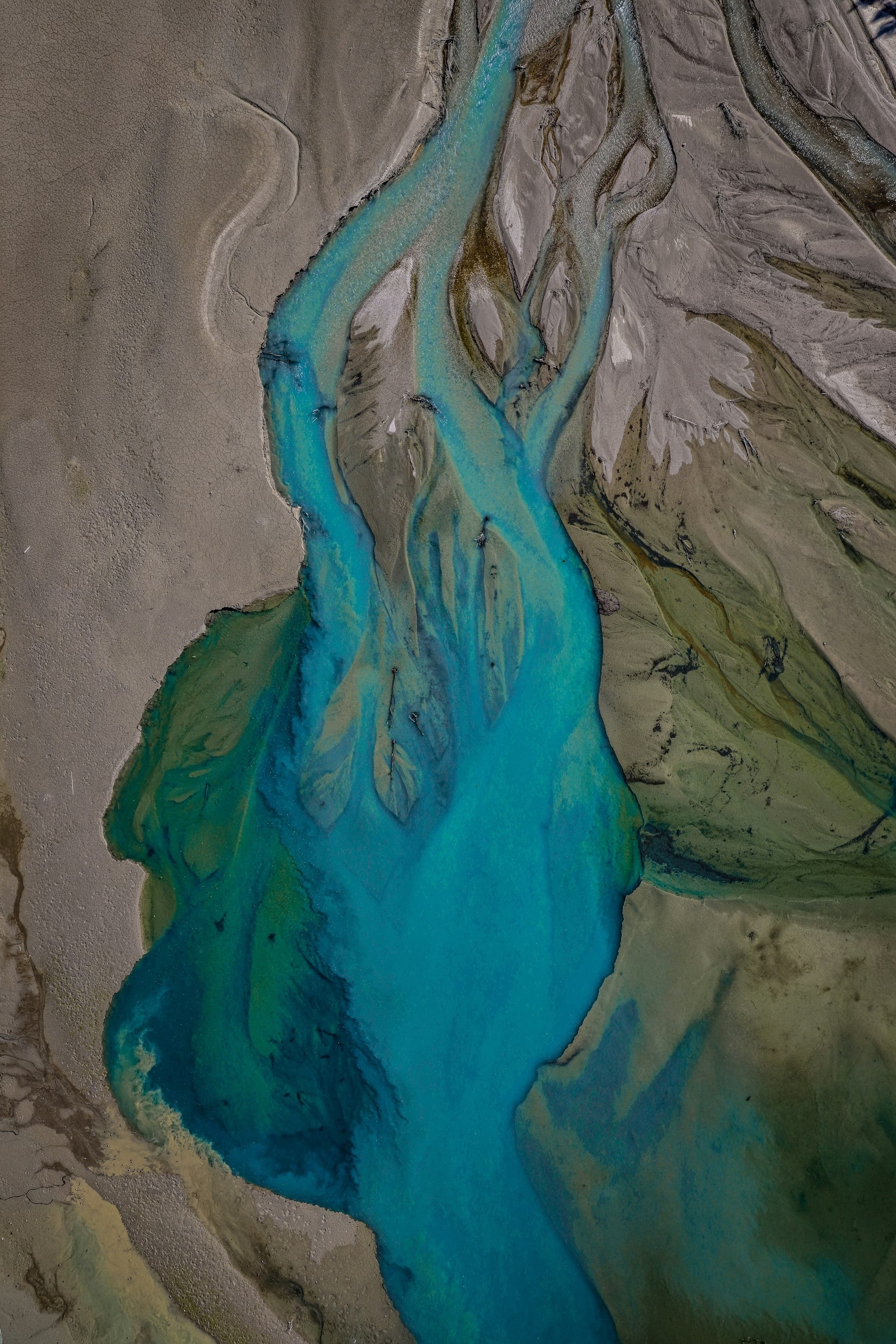 Aerial photograph of a braided glacial river delta with vivid turquoise water threading through grey sediment flats
