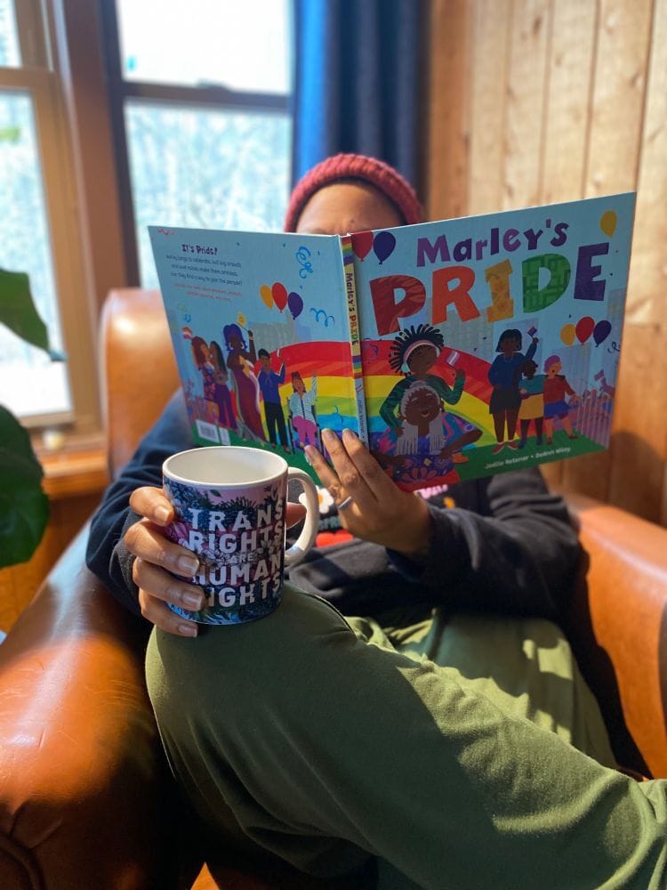 The author holding a copy of Marley's Pride up along with a mug that says Trans Rights are Human Rights