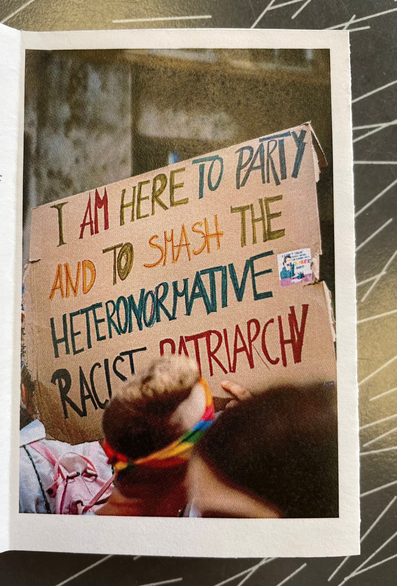 a colorful handwritten sign held up that says: I am here to party and to smash the heteronormative racist patriarchy