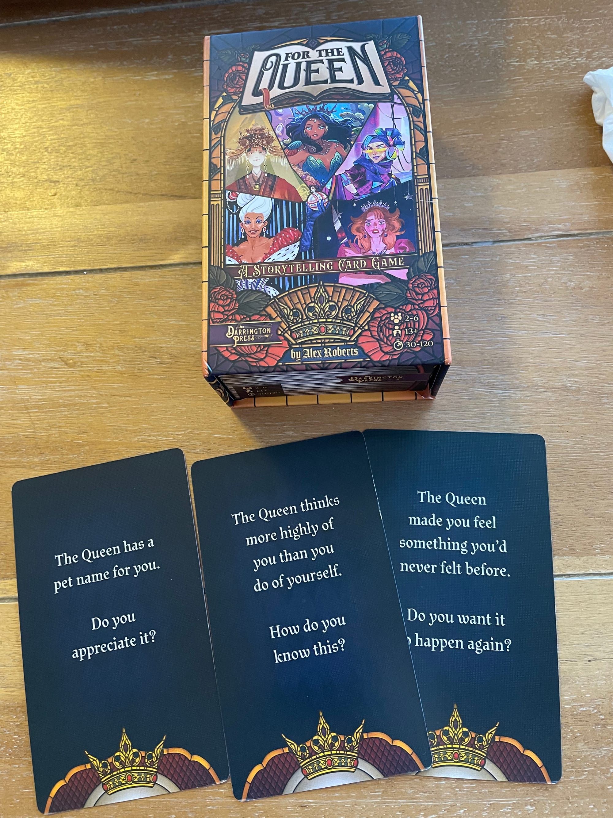 Sample cards from For The Queen, including the question "The Queen thinks more highly of you than you do of yourself. How do you know this?traveling this week, if needed can be reached via Teams and possibly take on minor tasks"