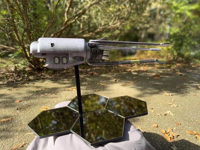 a handbuilt silver ship model sitting on a stand made of four hexagonal mirrors