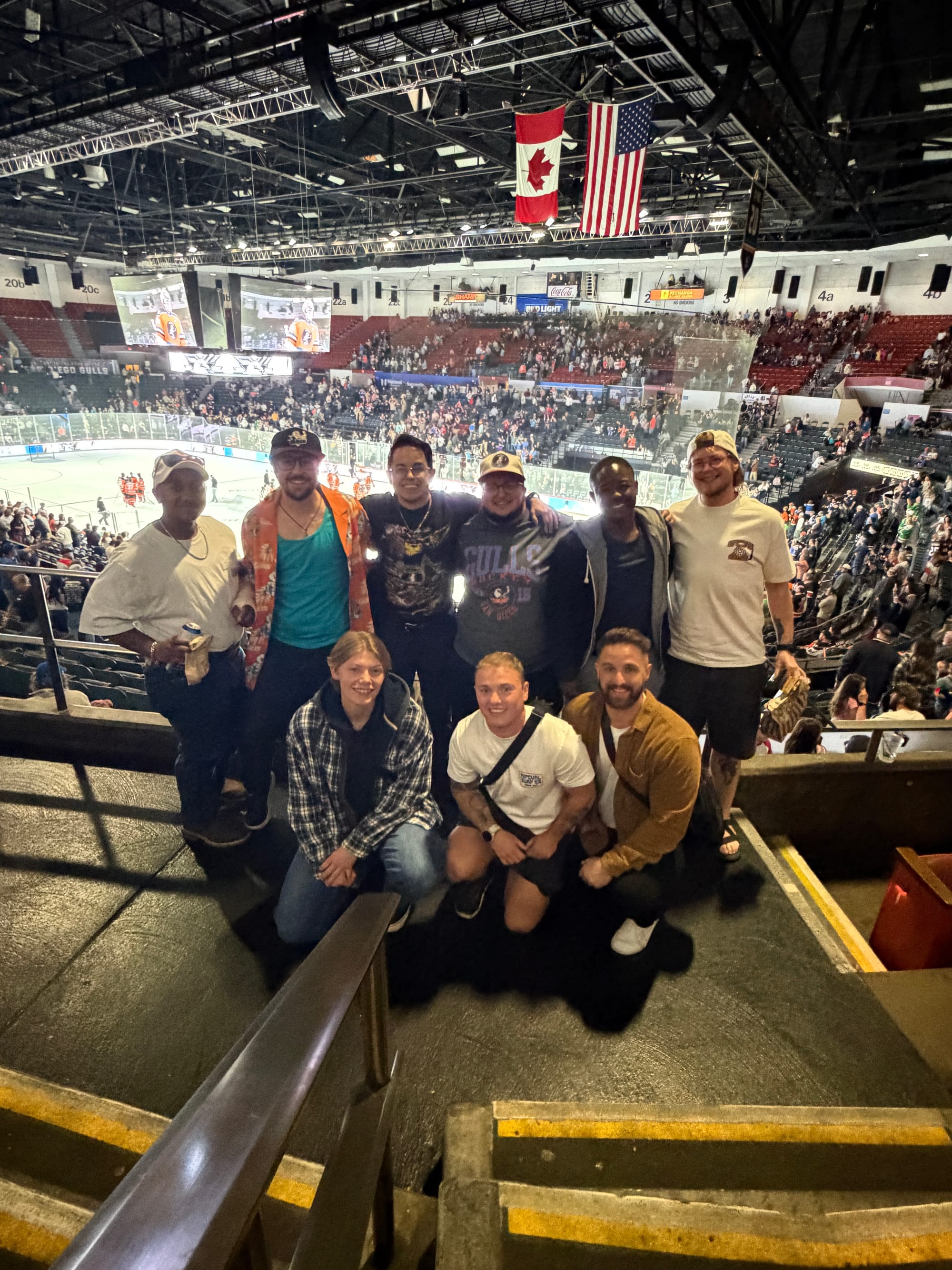 A group of nine transmasc people pose in front of a hockey rink