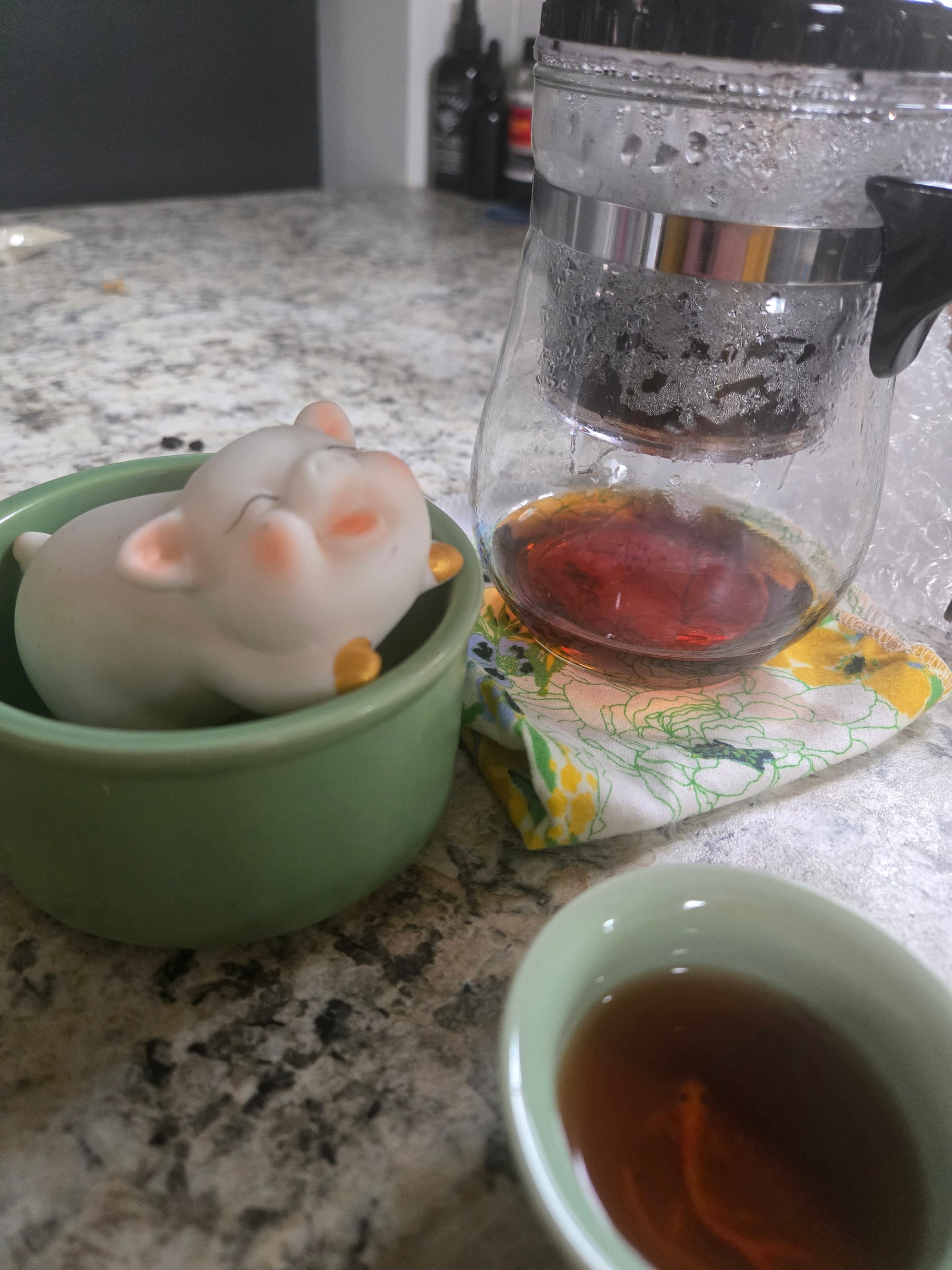 A plastic tea steeper, a white tea pig pet poking out of a saucer, and a mint tea cup with a koi fish on the bottom