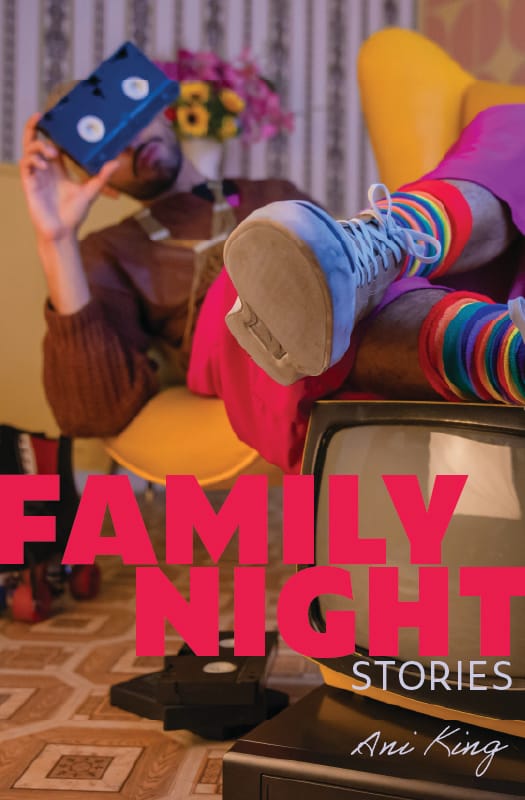 Family Night official book cover, which features a person with a mustache and short beard reclining in a yellow chair and holding a VHS tape over the top of their face so the white spool pieces look like eyes. They are wearing rainbow striped socks and lace up shoes, with their feet resting on a vintage television set. A small pile of VHS tapes rests on the floor, and FAMILY NIGHT stretches across the cover image in bright pink capitals, with Stories and Ani King in underneath in smaller, light blue font.