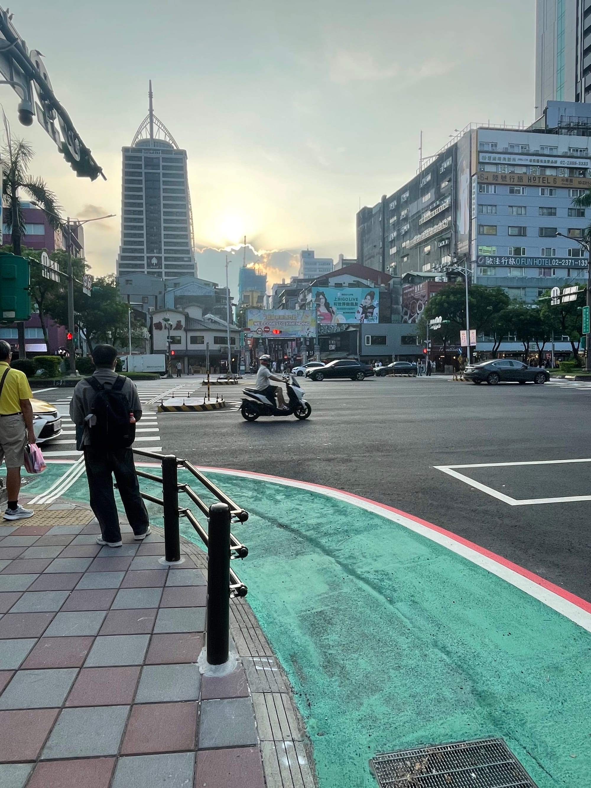 A colorful sidewalk before the entrance to Ximending, the queer neighborhood of Taipei. Sun shines behind cool clouds on the horizon.