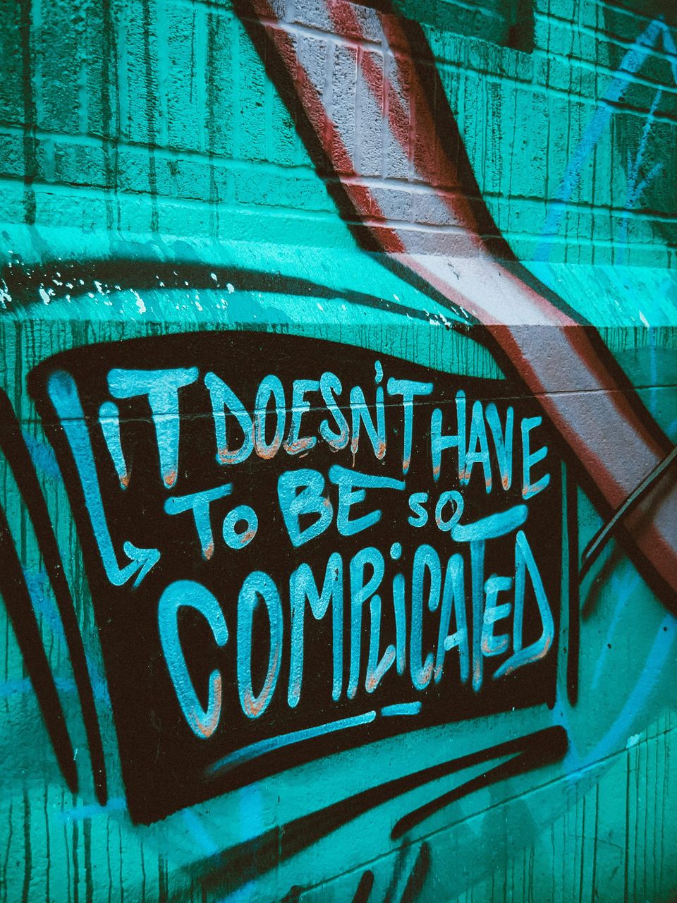 black graffiti on a turquoise wall that reads It Doesn't Have To Be So Complicated