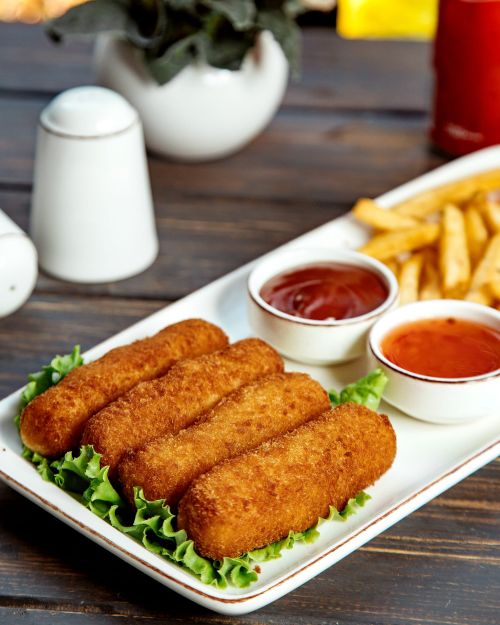 A plate with fishfingers, chips and a pot of sauce.