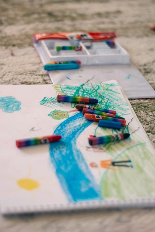 A crayon drawing of a house and trees with crayons lying on top of it.