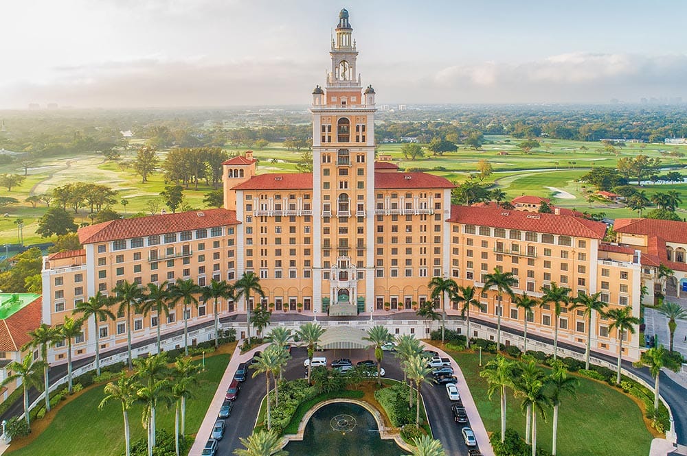 Aerial view of the historic Biltmore Hotel in Coral Gables with its iconic tower and resort pool surrounded by lush greenery.