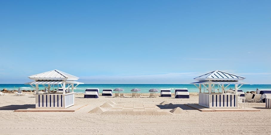 The Miami Beach EDITION private beach with striped cabanas and umbrellas facing the Atlantic.
