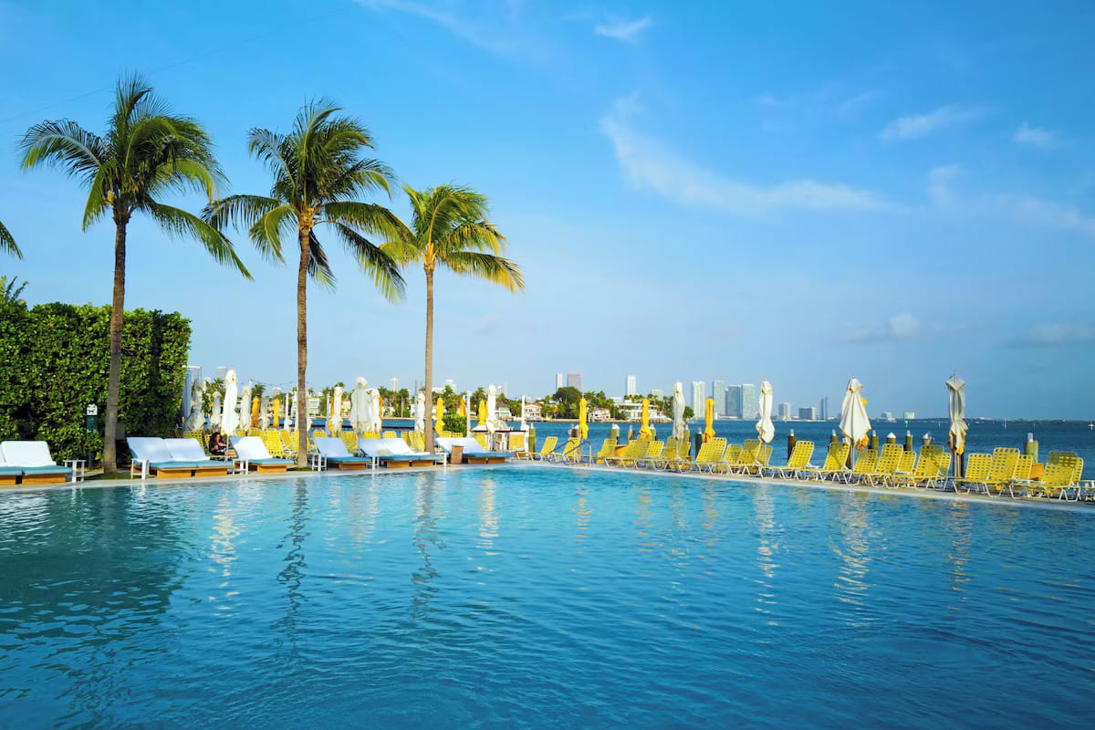 Saltwater infinity pool at The Standard Spa, Miami Beach framed by yellow umbrellas, palms, and a sunset skyline over Biscayne Bay.