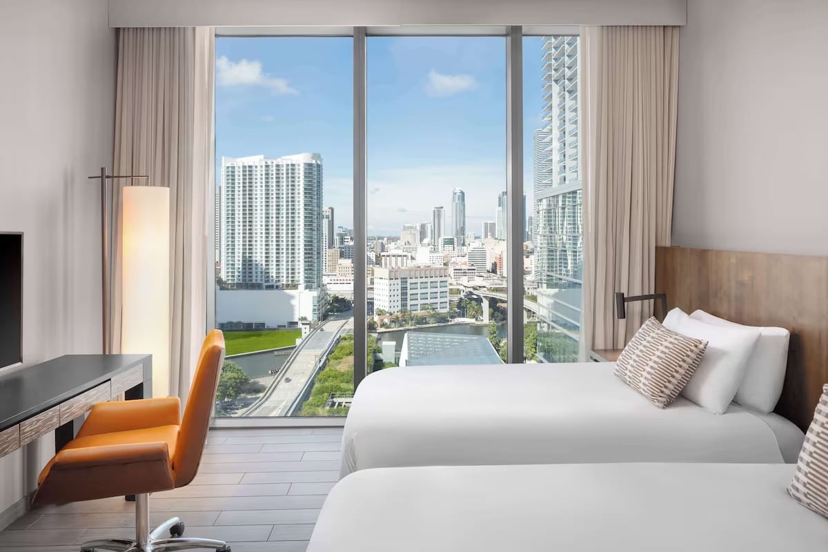 Modern double bedroom at EAST Miami in Brickell with floor-to-ceiling windows, city skyline views, luxury bedding, and minimalist design.