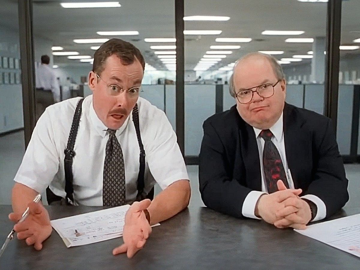 A still from a well-known scene in the movie "Office Space" with two consultants asking an employee what he actually does at the company.
