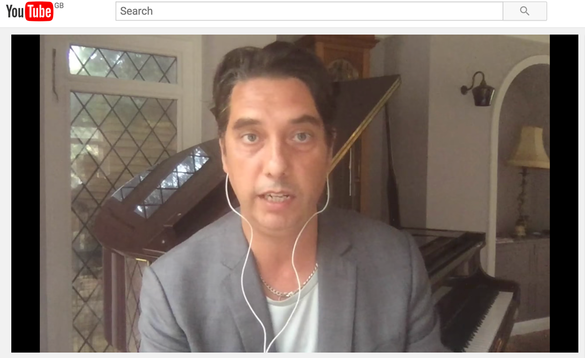 A YouTube screenshot of Elliott King in a grey blazer and wired earphones live streaming beside a piano.