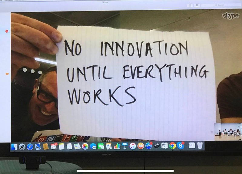 A man on a Skype call holds up a piece of paper on which is written "no innovation until everything works"