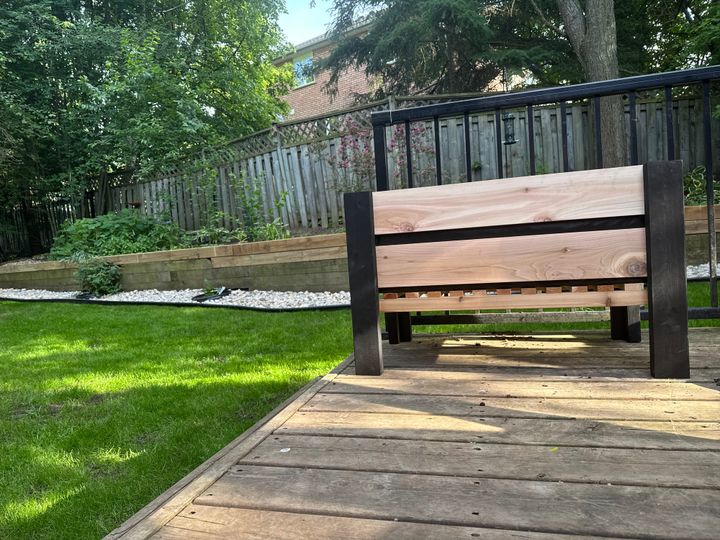 Picture of a planter box on a deck, grass and a fence in the background.