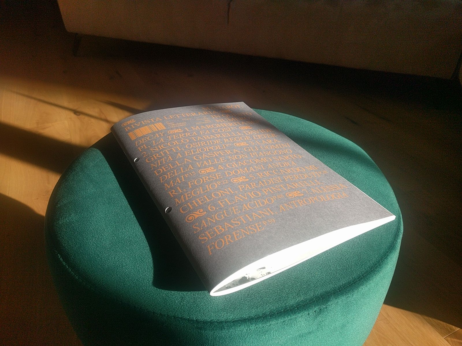Immagine della rivista appoggiata su un puff verde.