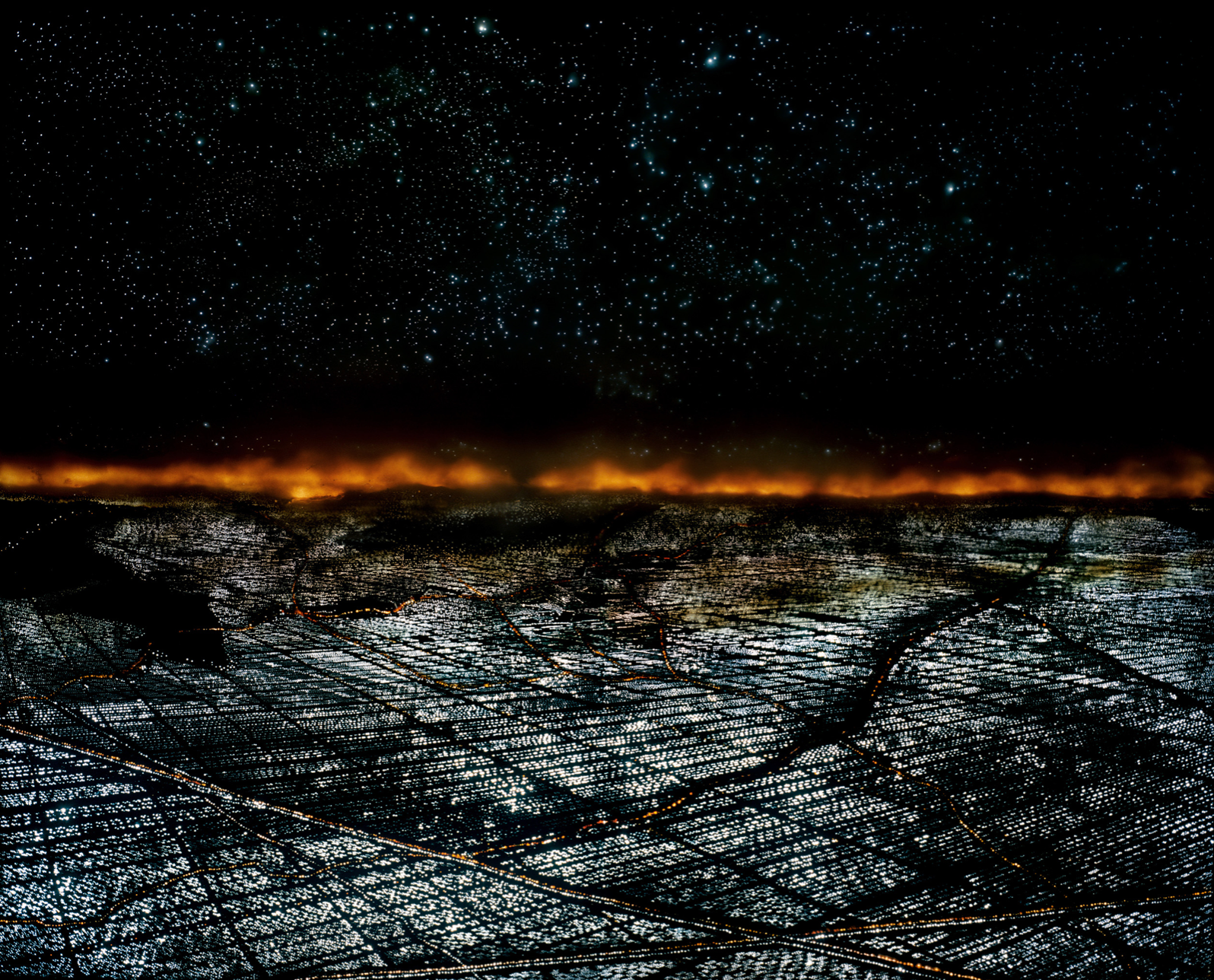 Una città vista dall'alto, di notte, con un incendio all'orizzonte.