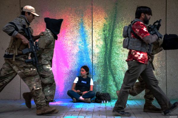 Frame tratto dal film Civil War: una reporter siede appoggiata a un muro, mentre due soldati conducono via dei prigionieri.